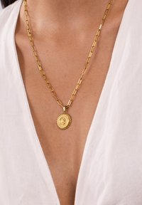 Goldene Halskette mit verlängerten Gliedern, versehen mit einem runden Anhänger mit detaillierter, seilartiger Textur und zentralem Motiv.