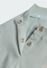 Polo in cotone verde chiaro con chiusura a scatto, collo a costine e tessuto strutturato. Presenta bottoni a pressione in metallo e dettaglio con logo.