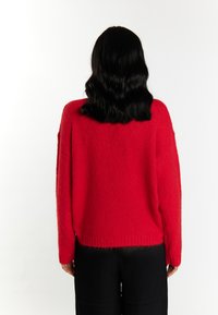 Maglione rosso, con texture, dal fit rilassato, con bordo a coste e maniche lunghe, visto da dietro su uno sfondo bianco.