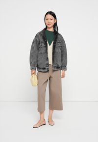 Casaco de denim cinza oversized, t-shirt verde, cardigan bege, calças largas bege, sapatilhas rosas e uma bolsa amarelo-claro. Fundo branco liso.