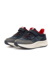 Marineblaue und graue Sportschuhe mit roten und weißen Akzenten, ausgestattet mit einem Klettverschluss und strukturierten Sohlen für besseren Halt.