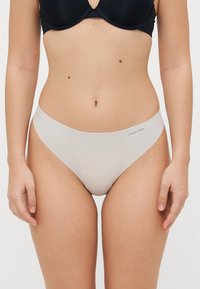 Lichtgrijze Calvin Klein stringonderbroek met een gladde textuur, lage taille en minimale branding bij de tailleband.