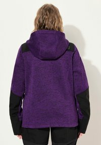 Giacca in pile viola con finitura testurizzata, dettagli neri su spalle e maniche, e cappuccio. Presenta una vestibilità ampia.