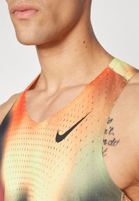 Nike Sporttanktop mit einem Farbverlauf von Orange zu Grün, V-Ausschnitt und perforierter Textur. Schwarzes Logo auf der Vorderseite sichtbar.