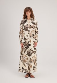 Ensemble composé d'un chemisier à manches longues et d'une jupe maxi en crème avec de grands motifs floraux marron. Fabriqué en tissu léger ; présente un devant à boutons.