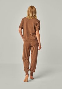 Brown knit loungewear set featuring a short-sleeve top and tapered pants with cuffed ankles, smooth texture, and relaxed fit.