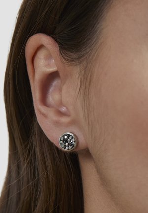 Runde Ohrstecker mit metallischem Rand, verziert mit Clustern aus reflektierenden schwarzen und silbernen Steinen, getragen am Ohr einer Person.