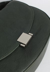 Borsa in pelle verde con un flap arrotondato, dotata di una chiusura metallica quadrata e cuciture a contrasto. Superficie testurizzata con logo del marchio impresso.