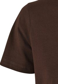 Gros plan sur un t-shirt en coton marron uni à manches courtes montrant la texture du tissu et la couture de l'ourlet de la manche.