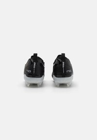 Black soccer cleats with a glossy finish. Features a curved design, rubber soles, and rear pull tabs for easy wear. "Joma" branding visible.
