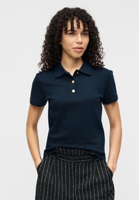 Polo bleu marine avec un col à revers, trois boutons dorés et des manches courtes, associé à un pantalon à fines rayures. Texture lisse.