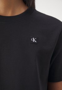 Svart bomull t-shirt med rund hals och korta ärmar, med en liten broderad vit 'cK'-logotyp på vänster bröst.