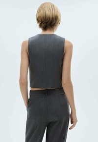 Grijs cropped mouwloos topje met verticale streepjes, aangevuld met getailleerde grijze broek, die een strakke, minimalistische uitstraling toont.