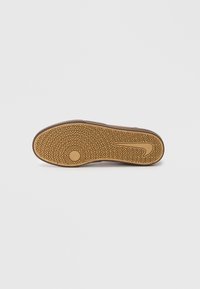 Shoe sole with a rubber material, featuring a zigzag pattern, circular accent, and a logo imprint. Color is brown with a textured finish.