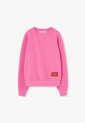Sudadera de forro polar rosa con cuello redondo, mangas raglán, puños y cinturilla de canalé. Presenta una etiqueta de logo roja en la parte inferior izquierda.