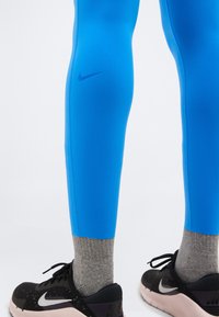 Πόδια με φωτεινά μπλε κολάν Nike, γκρι κάλτσες και μαύρα παπούτσια τρεξίματος Nike με λευκές σόλες και λογότυπα swoosh.