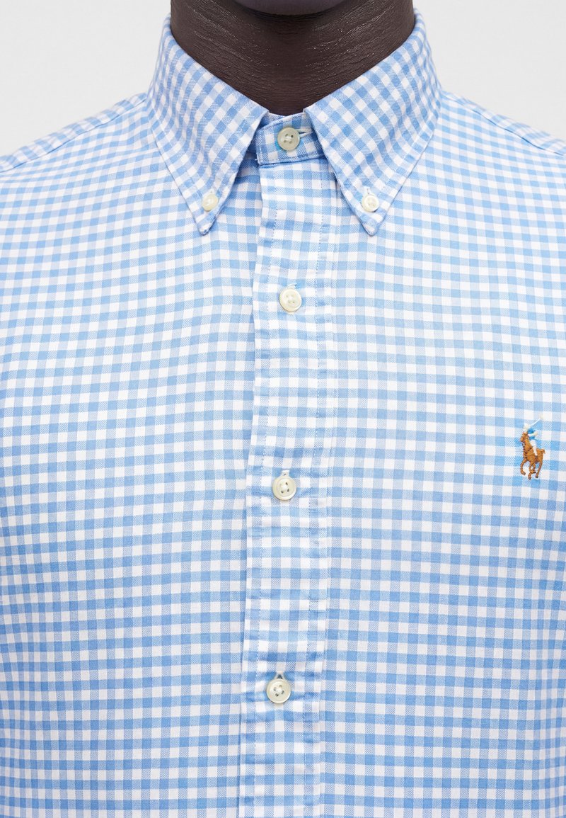 Chemise à carreaux bleue et blanche à boutons, col boutonné et petit logo brodé sur la poitrine gauche.