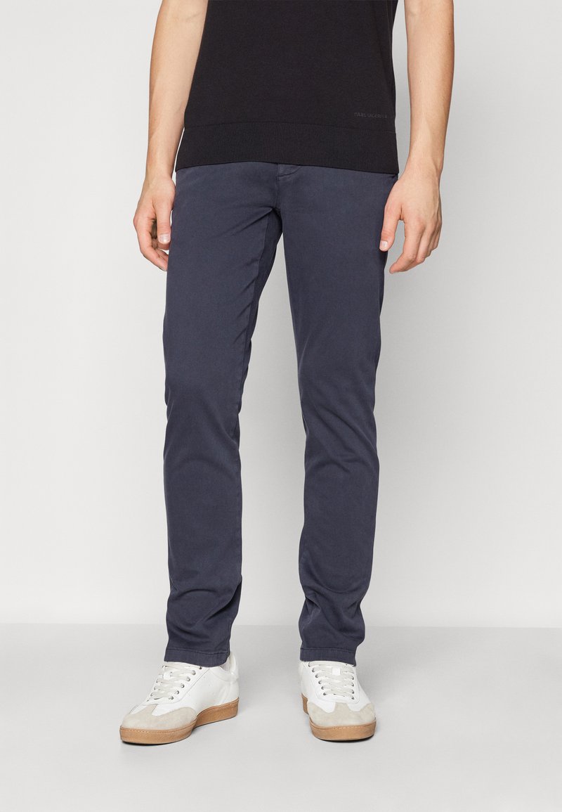 Chinos in cotone blu navy con una vestibilità slim, caratterizzati da una texture liscia e tasche standard, abbinati a sneakers bianche.