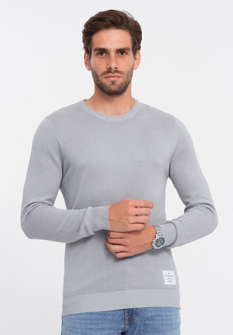 Hellgrauer Strickpullover mit strukturierter Oberfläche, Rundhalsausschnitt, gerippten Bündchen und Saum. Weist ein kleines Markenlabel an der unteren Seite auf.