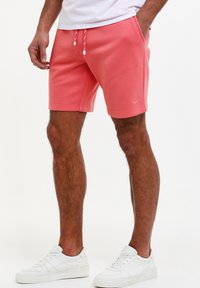 Bermudas de color coral hechas de material suave, con una cinturilla elástica con cordones, bolsillos laterales y un logo sutil en la pierna.