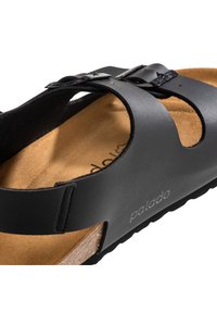 Sandalia de cuero negro con diseño recortado y hebilla ajustable. Plantilla de corcho natural y suela de goma texturizada. Superficie lisa.