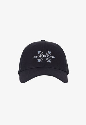 Homme aux cheveux bouclés portant une casquette noire ornée de feuilles bleues et un t-shirt noir avec un petit logo géométrique blanc sur la poitrine.