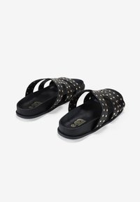 Sandalias de slide negras con correas entrecruzadas, con acentos de tachuelas doradas y una suela de textura lisa. Diseño minimalista, estilo de punta abierta.