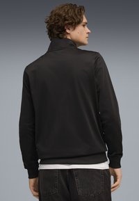 Giacca nera leggera con colletto alto, polsini e orlo a coste. Texture liscia, design semplice e senza loghi o motivi visibili.