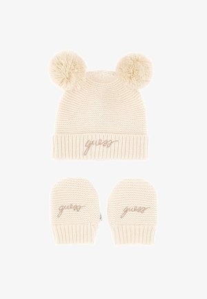 Bonnet en tricot crème avec deux pompons et un poignet côtelé, ornée d'un logo "guess" en rose gold. Une paire de mitaines en tricot assorties est incluse.