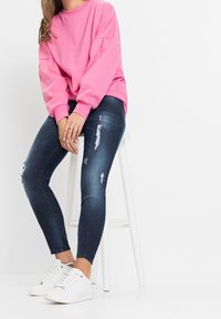 Růžová oversized mikina, tmavé roztrhané skinny džíny a bílé tenisky. Hladké materiály, volný střih a minimalistický design.