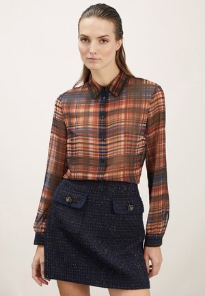 Chemise à manches longues à carreaux orange, marron et bleu, avec un devant à boutons et un col, associée à une jupe bleue marine texturée dotée de deux poches.
