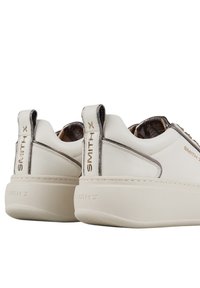 Sneakers bianchi in pelle con suola spessa, caratterizzati da dettagli metallici e linguette marchiate. L'interno è decorato con un motivo e ha una texture particolare.