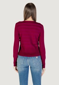 Maglione fitted color bordeaux con maniche lunghe e texture rigata orizzontale. Abbinato a jeans in denim fitted di colore azzurro chiaro.