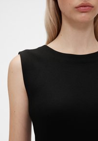 Melna bezroku blūze ar apaļu kakla izgriezumu. Izgatavota no mīksta auduma ar gludu tekstūru un minimālām šuvēm uz pleciem.
