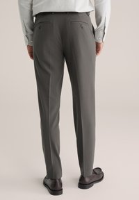 Sive hlače z ravnim krojem, dvema zadnjima žepoma in rjavimi gumbnimi detajli, v kombinaciji s črnimi poslovnimi čevlji.