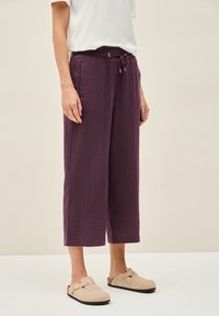 Pantalons courts texturés violets avec une taille à cordon de serrage et des poches latérales, associés à des sabots en suede légers et à enfiler.