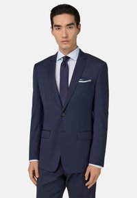 Tamsiai mėlynas kostiumas su vieno mygtuko uždarymu, notch tipo apykaklėmis ir dviem priekiniais kišenėmis. Baltas dryžuotas marškinis ir deranti kaklaraištis papildo išvaizdą.