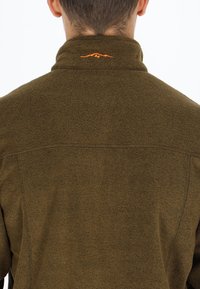 Giacca in pile verde oliva con collo alto, caratterizzata da un dettaglio del logo arancione sul retro e una superficie morbida e testurizzata.