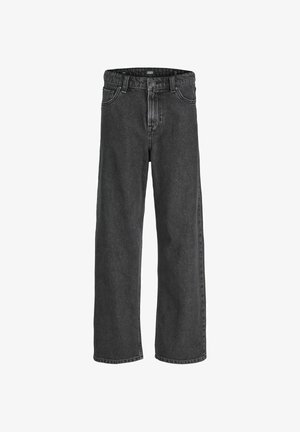 Chłopiec stoi i się uśmiecha, ubrany w beżową kurtkę na niebieskiej flanelowej koszuli, ciemnoszare spodnie i jasnobrązowe buty, na jednolitym tle.