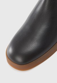 Bottine en cuir noir avec un dessus texturé, bout rond et semelle en caoutchouc marron contrastante. Fini lisse et design sans coutures.