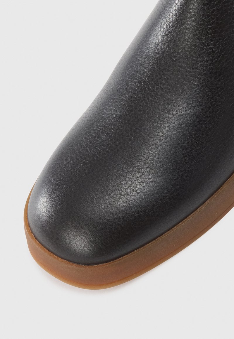Schwarze Leder-Ankle-Boots mit einer strukturierten Oberfläche, runder Spitze und einer kontrastierenden braunen Gummisohle. Glatte Oberfläche und nahtloses Design.