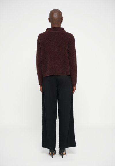 Bordo pullover kõrge kraega, pehmest materjalist, koos mustade laiade pükstega ja mustade kõrge kontsaga kingadega.