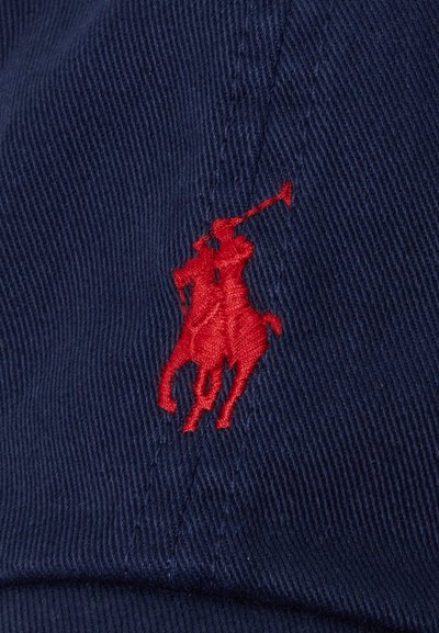 Marinen cap har en fremtredende rød broderte logo av to ryttere på hesteryggen. Stoffet har en teksturert overflate.