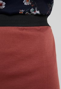 Primo piano della vita che indossa un top floreale nero infilato in una gonna alta color rosa polveroso con una fascia elastica nera in vita.