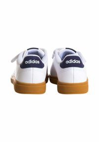 Zapatillas blancas con un upper de cuero suave, tab de talón en color azul marino y suela de goma. Presenta un branding mínimo en blanco en el talón.