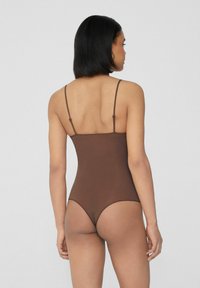 Hnědý body s tenkými ramínky, bezešvý design a hladká textura. Má vysoký střih nohavic a minimalistický styl zad.