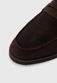 Brown suede loafers with a rounded toe, visible stitching, and a textured surface. Flexible black rubber sole adds grip and comfort.