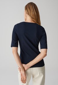 Top a maniche corte blu navy realizzato in tessuto morbido, con scollatura a giro e vestibilità slim, abbinato a pantaloni chiari.