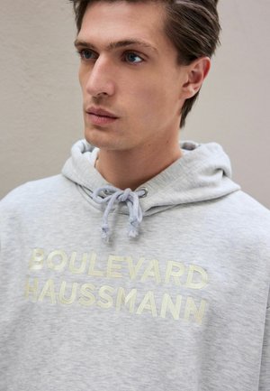 Grey hoodie with drawstring, featuring metallic text "BOULEVARD HAUSSMANN" on the front. Soft texture, casual design, relaxed fit.