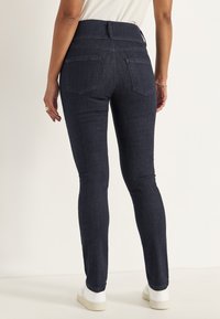 Mörkblå skinny jeans av denim med hög midja, två bakfickor och en mjuk yta, tillsammans med vita sneakers.